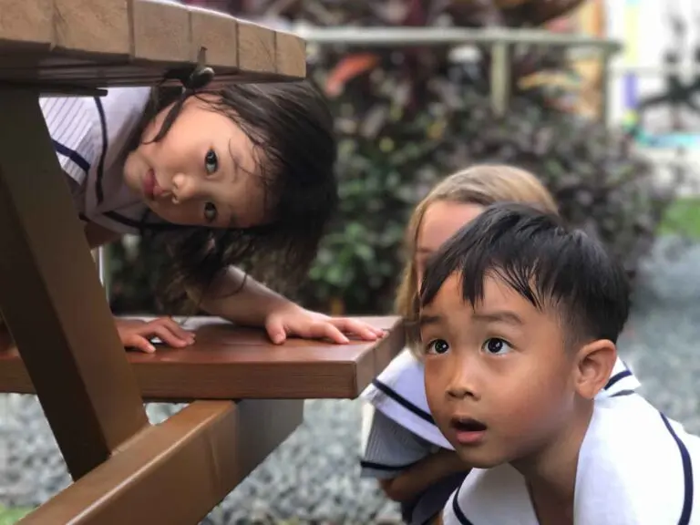 Children exploring and playing under a table outdoors at preschool