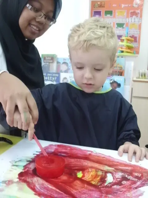 老师在一次红色绘画活动中引导一名幼儿园孩子。