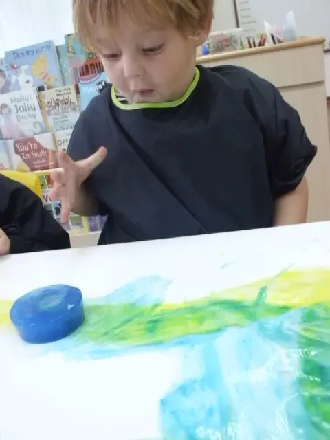 孩子在纸上尝试蓝色与绿色颜料。