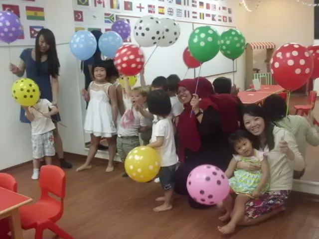 Children and teachers gathered indoors with bright balloons.