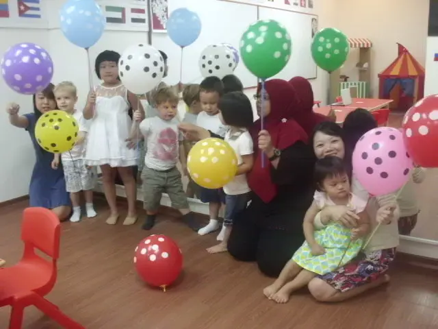 Preschool group posing with red, green, yellow and blue balloons.