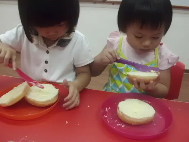 Two children preparing bread at a red classroom table.