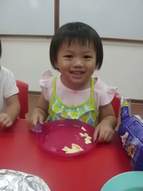Smiling preschool child seated with a plate of prepared food.
