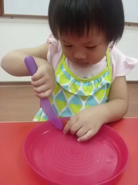 Young child concentrating while using a plastic knife on a plate.