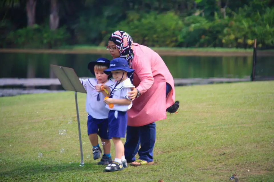 幼儿园的孩子在花园池塘旁吹泡泡。
