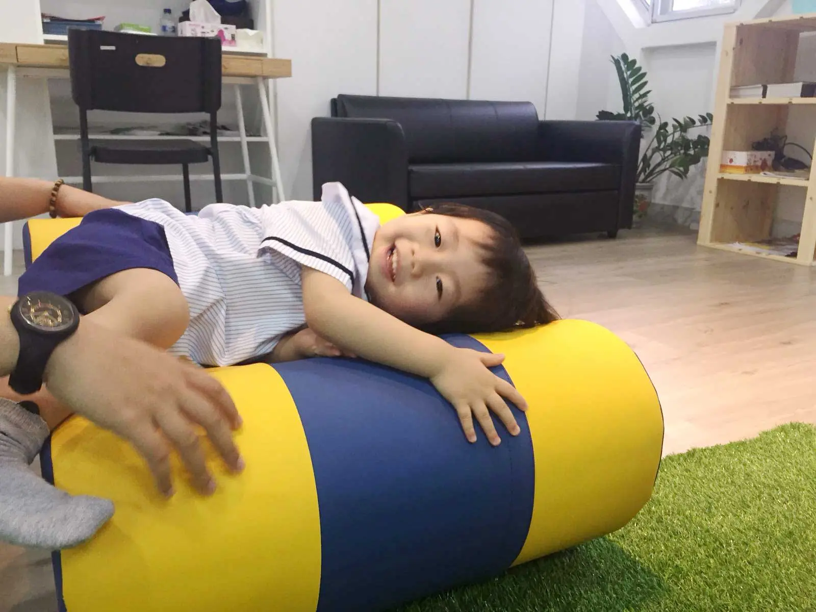 Preschool child lying across a soft blue and yellow play cylinder.