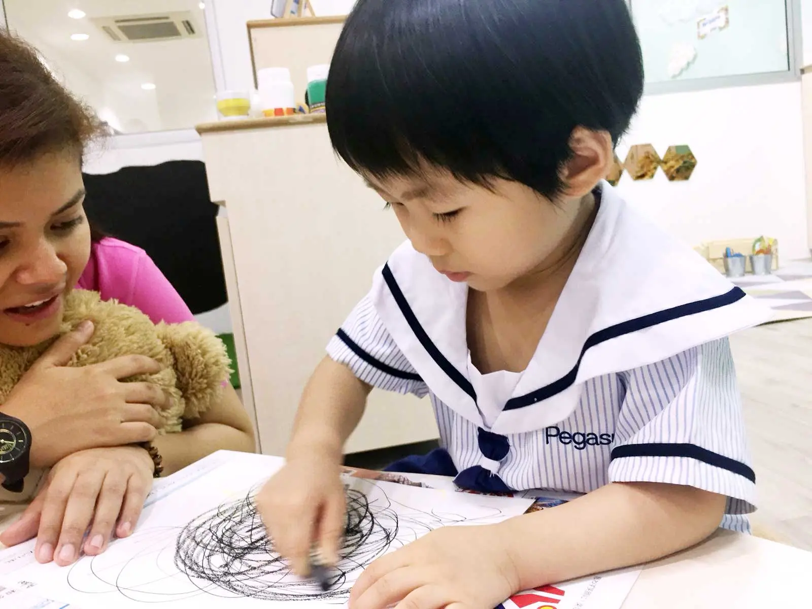 Child making bold circular scribbles while an adult observes.
