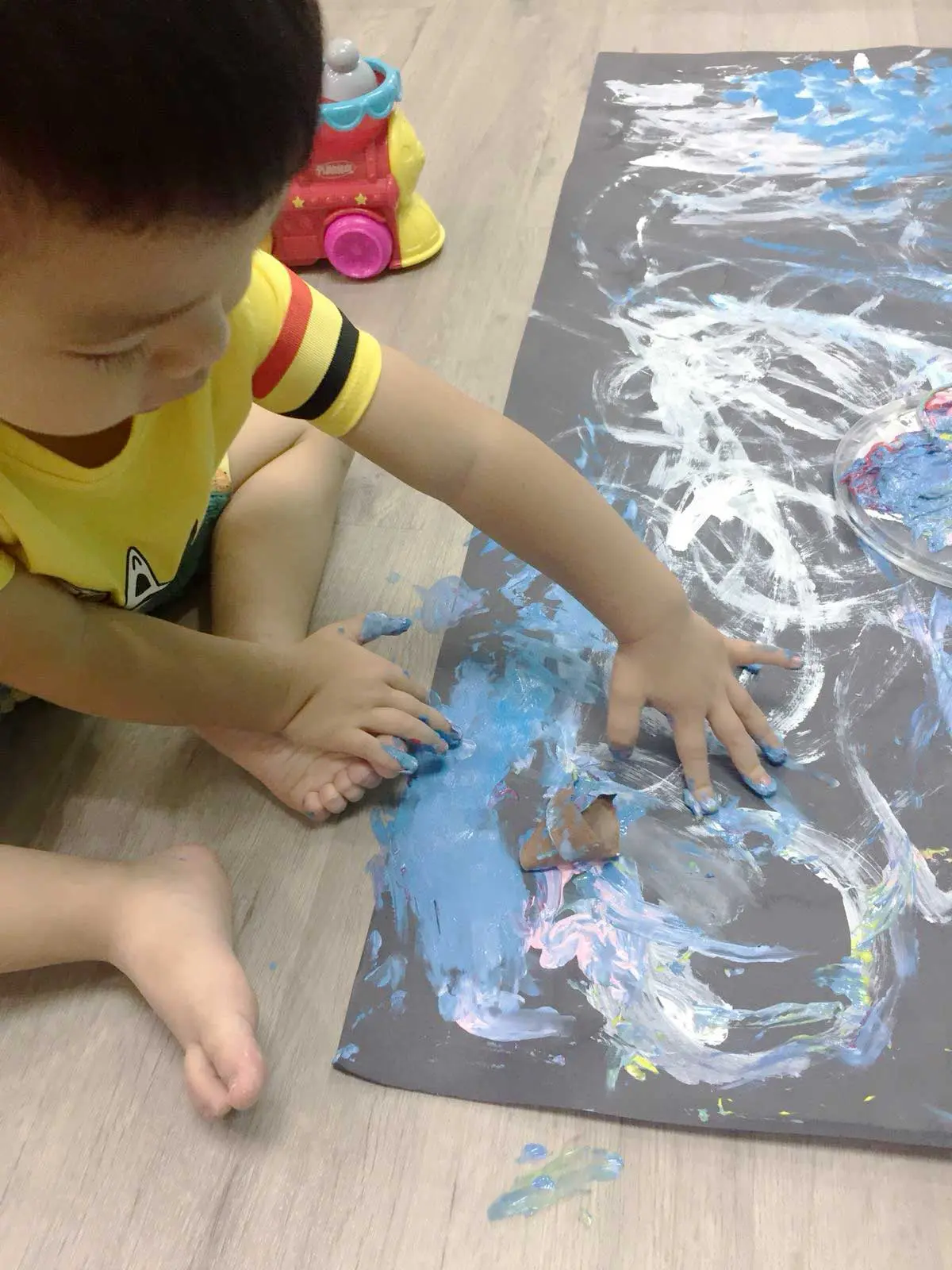 Child using both hands to spread blue and white paint on dark paper.