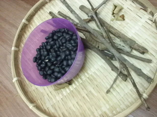 Black seeds and small branches displayed on a woven tray.