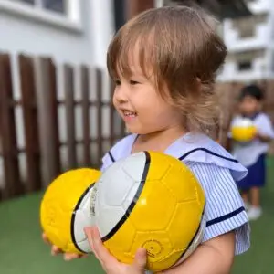 Nursery 1 child holding yellow soccer balls during preschool activity
